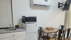 Een kleine keuken met een koelkast, een magnetron en een eettafel met stoelen.