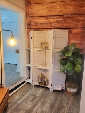 A white, multi-tiered storage unit with decorative items against a wooden wall.