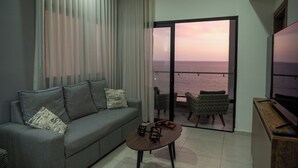 Ein modernes Wohnzimmer mit grauem Sofa, einem kleinen Couchtisch und einem Balkon mit Meerblick.
