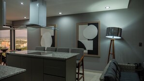 Eine moderne Küche mit einer zentralen Kochinsel, einem Essbereich mit Stühlen, einer Stehlampe und abstrakter Wandkunst.