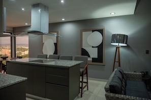 Eine moderne Küche mit einer zentralen Kochinsel, einem Essbereich mit Stühlen, einer Stehlampe und abstrakter Wandkunst.
