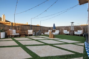Un patio trasero con valla de madera, mobiliario exterior e iluminación colgante.