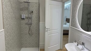 A bathroom with a shower, a sink, a mirror, and a door leading to a bedroom. - Emy Suites (Civitavecchia)