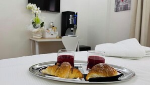 A hotel room with a bed, a tray with croissants and juice, a TV, a coffee machine, and a wall-mounted picture. - Emy Suites (Civitavecchia)