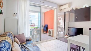 A modern apartment with a sofa, a TV, and a balcony with a table and chairs. - "Le Pajo" Seafront apartment, T3 Air-conditioned - Wifi, Swimming pool and parking lot (Sète)