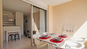 A dining area with a table set for four, a kitchen area with a microwave, and a sliding glass door leading to a balcony. - "Le Pajo" Seafront apartment, T3 Air-conditioned - Wifi, Swimming pool and parking lot (Sète)