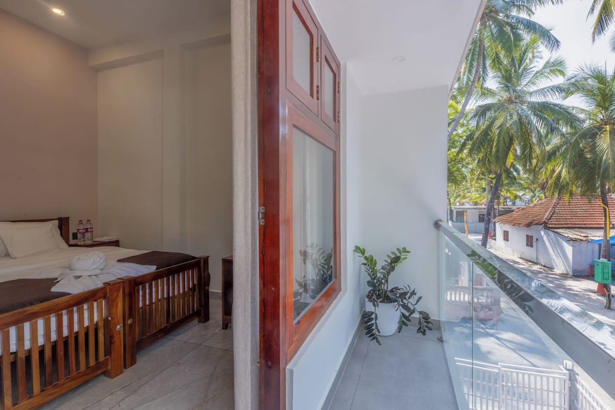 Une chambre d’hôtel avec un lit, un banc en bois, un balcon donnant sur des palmiers et une rue.