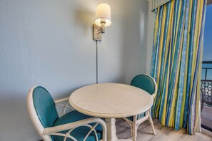 Une petite table ronde avec deux chaises, un luminaire fixé au mur et une fenêtre avec des rideaux à rayures.