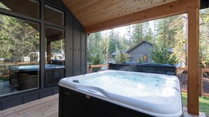 Een hottub op een houten terras met uitzicht op een huis en bos.