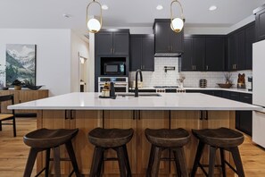 A modern kitchen with a large island, dark cabinetry, and a white countertop. - Mt Hood Cabin, Putting Green, Hot Tub, Pool Table, Sleeps 10, Pet Friendly (Mount Hood Village)