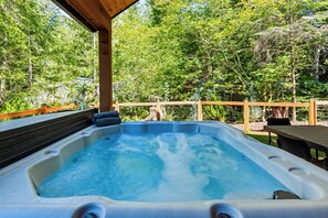 Een hottub met een houten terras en uitzicht op een bebost gebied.