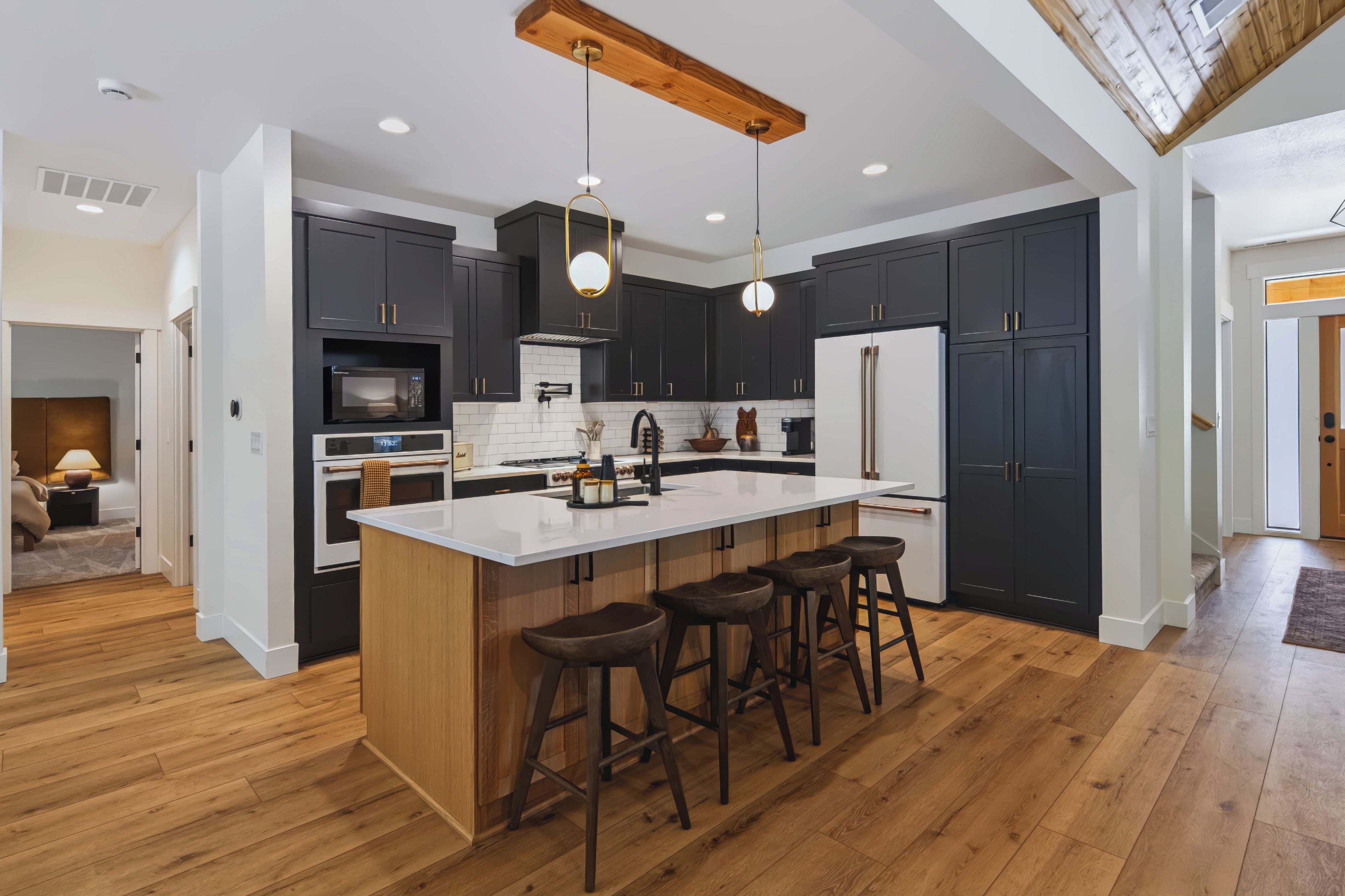 A modern kitchen with dark cabinetry, a central island with bar stools, and a wooden ceiling.