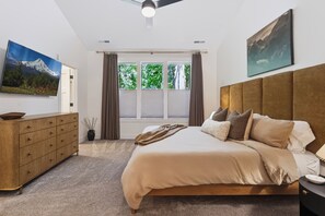 Een slaapkamer met een bed, een dressoir, een schilderij en een raam met gordijnen.