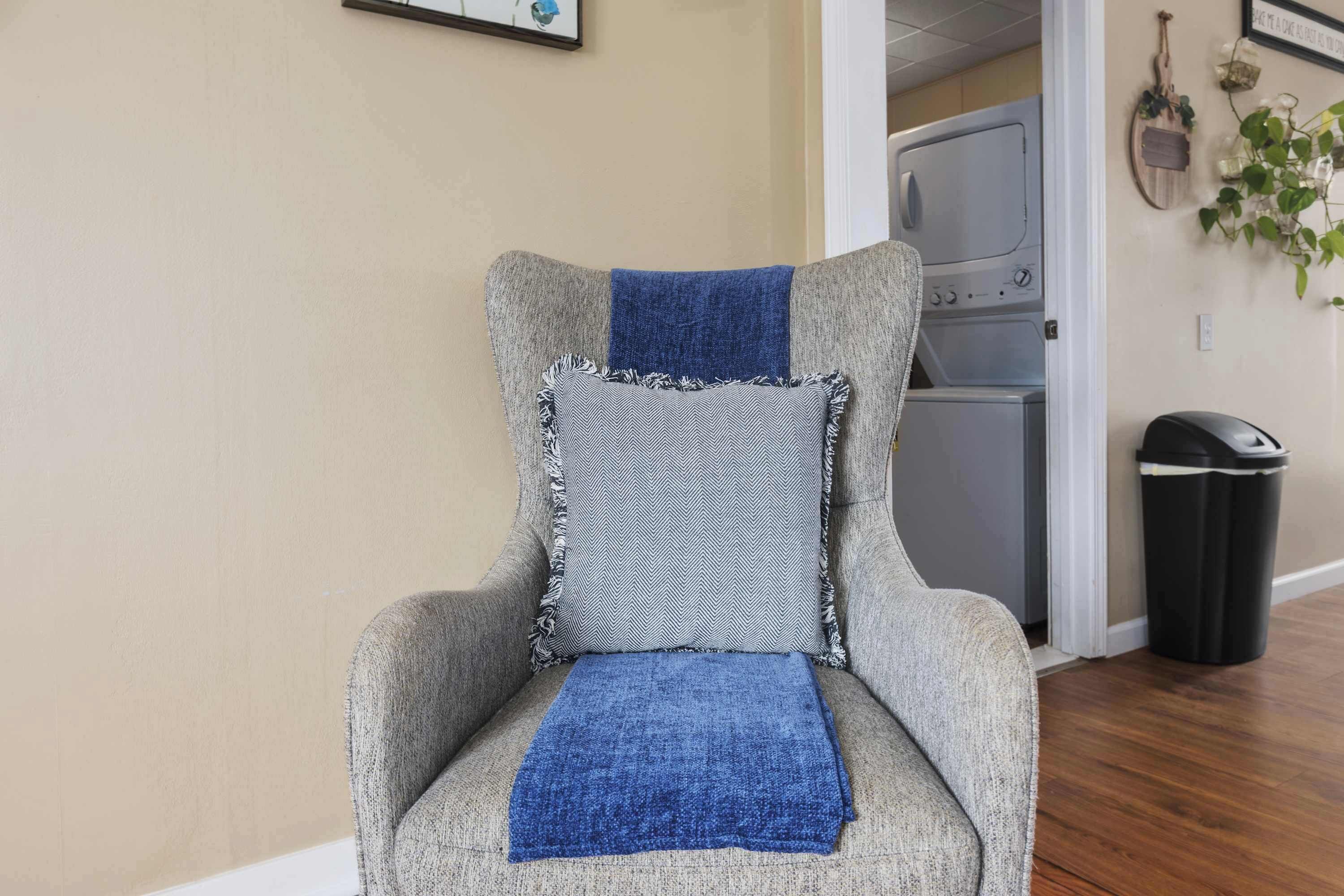 Un fauteuil gris avec un plaid bleu et un coussin à motifs.