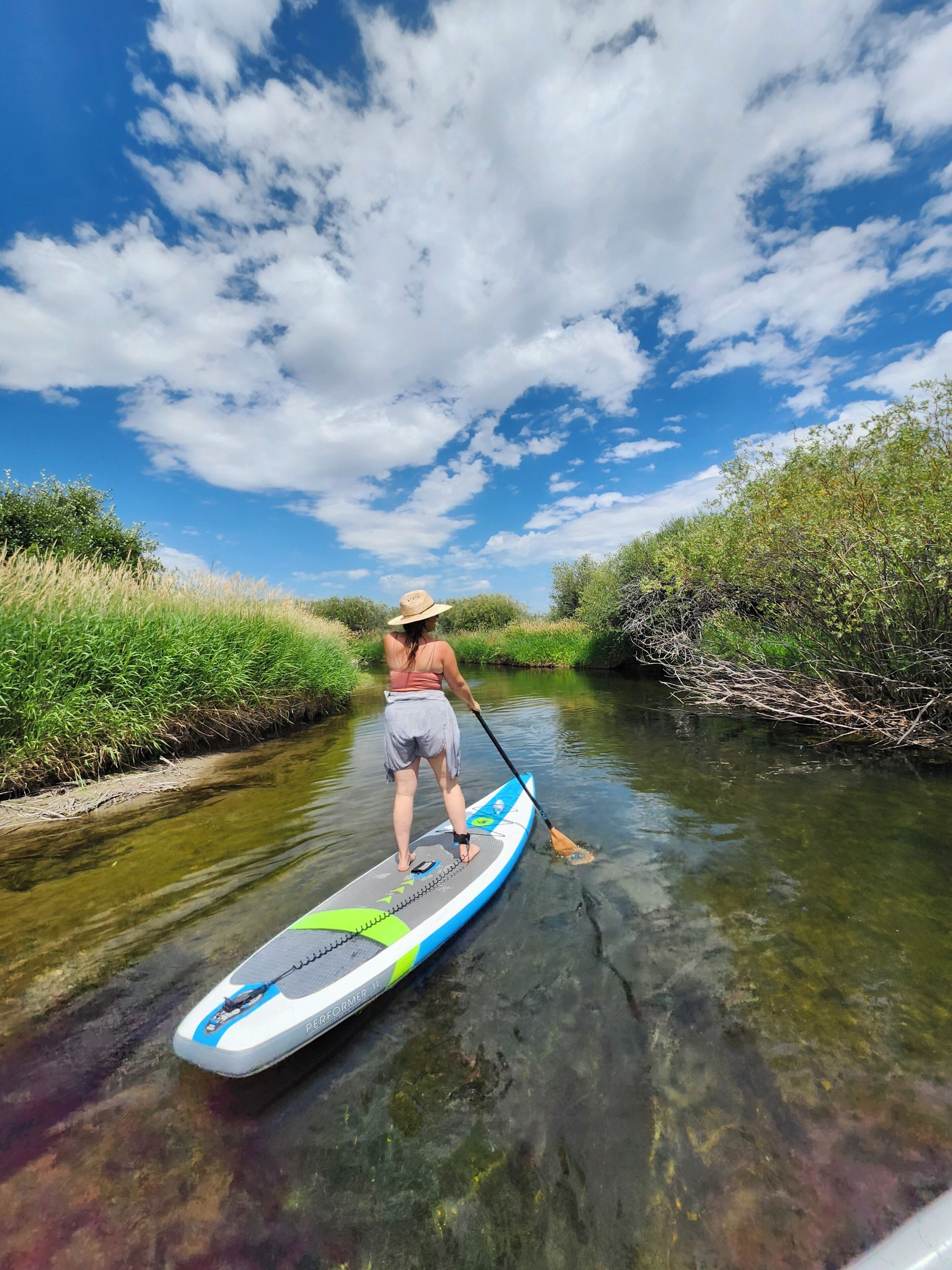 A person paddleboarding on a calm river surrounded by greenery.