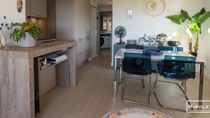 Ett modernt kök med träskåp, en inbyggd diskmaskin och en matplats med ett glasbord och metallstolar.