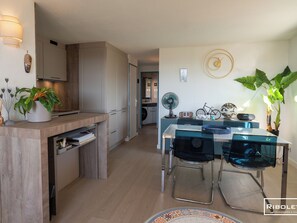 Eine moderne Küche mit Holzschränken, einem eingebauten Geschirrspüler sowie einem Essbereich mit Glastisch und Metallstühlen.