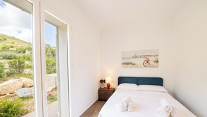 A bedroom with a bed, a nightstand, a lamp, and a painting of a bicycle on a beach. - Villa Manù - Sicilian Charm Retreat (Sicilia)