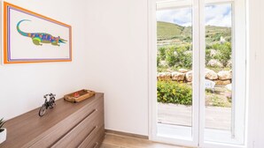 A room with a wooden dresser, a framed artwork of a lizard, and a view of a garden through a sliding glass door. - Villa Manù - Sicilian Charm Retreat (Sicilia)