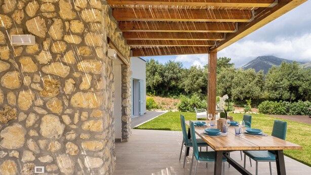 A stone exterior wall, a wooden pergola, a dining table with chairs, and a view of a mountain. - Villa Manù - Sicilian Charm Retreat (Sicilia)