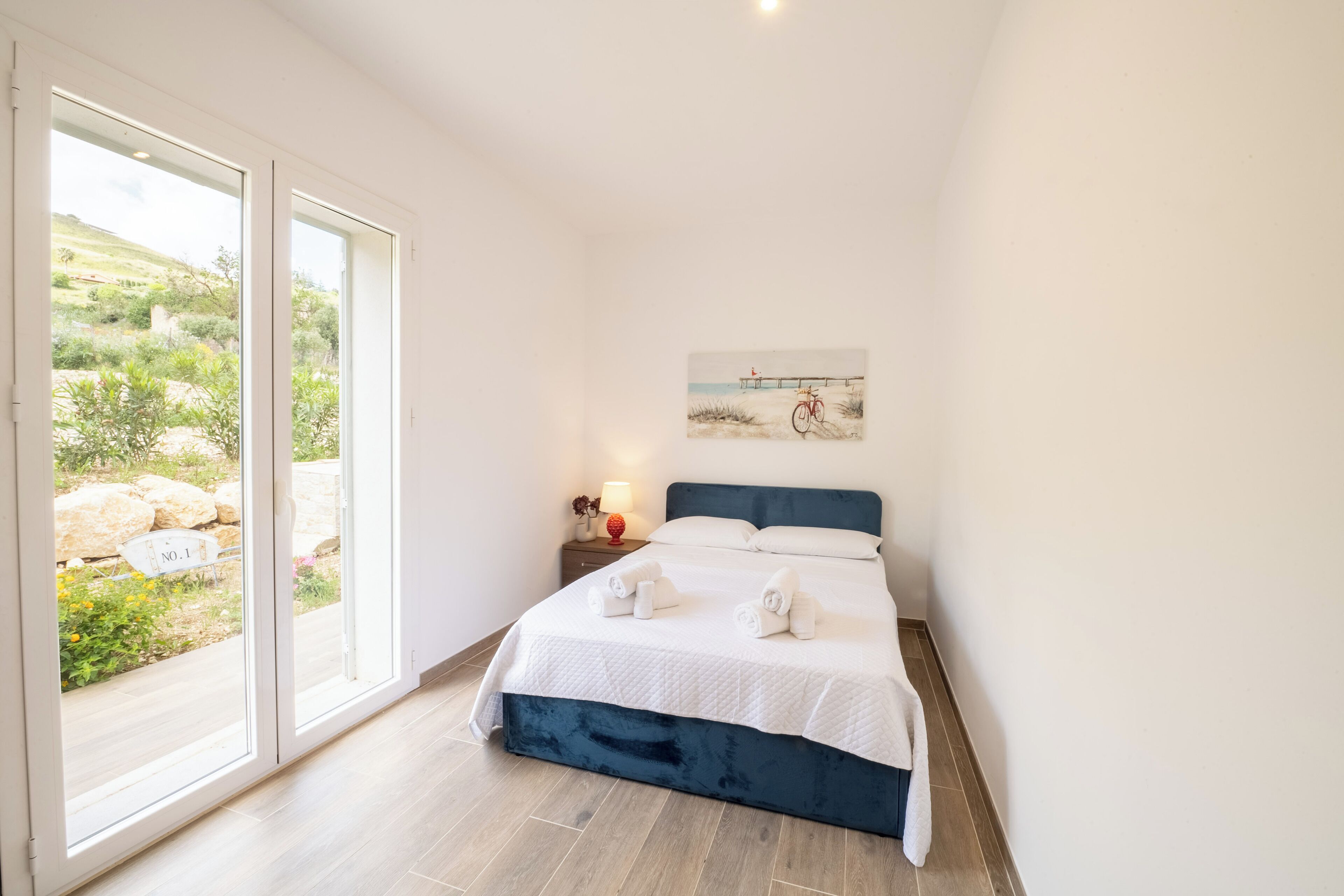 Een slaapkamer met een bed, een nachtkastje, een schilderij en uitzicht op het landschap.
