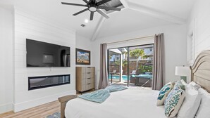 Ein Schlafzimmer mit einem großen Bett, einem an der Wand montierten Fernseher, einem Kamin und Blick auf einen Pool und Außenbereich.