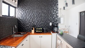 A modern kitchen with a black textured backsplash, wooden countertops, and white cabinets. There is a coffee maker, a knife block, and a fruit bowl on the counter. - Comfort apt in Oaxaca centro | Large kitchen, TV room + 100MB internet + KS bed (Oaxaca de Juárez)