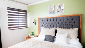 A bedroom with a large bed, a nightstand, a wall-mounted lamp, and two framed pictures on the wall. - Comfort apt in Oaxaca centro | Large kitchen, TV room + 100MB internet + KS bed (Oaxaca de Juárez)