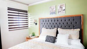 Ein Schlafzimmer mit einer gepolsterten Kopfteile, einem Bett mit weißer und gemusterter Bettwäsche, einem Nachttisch mit Lampe und zwei gerahmten Bildern an der Wand.