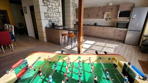 Ein Zimmer mit Kicker, Holzschränken, einer Steinwand und einer Küchenzeile mit Kühlschrank und Backofen.