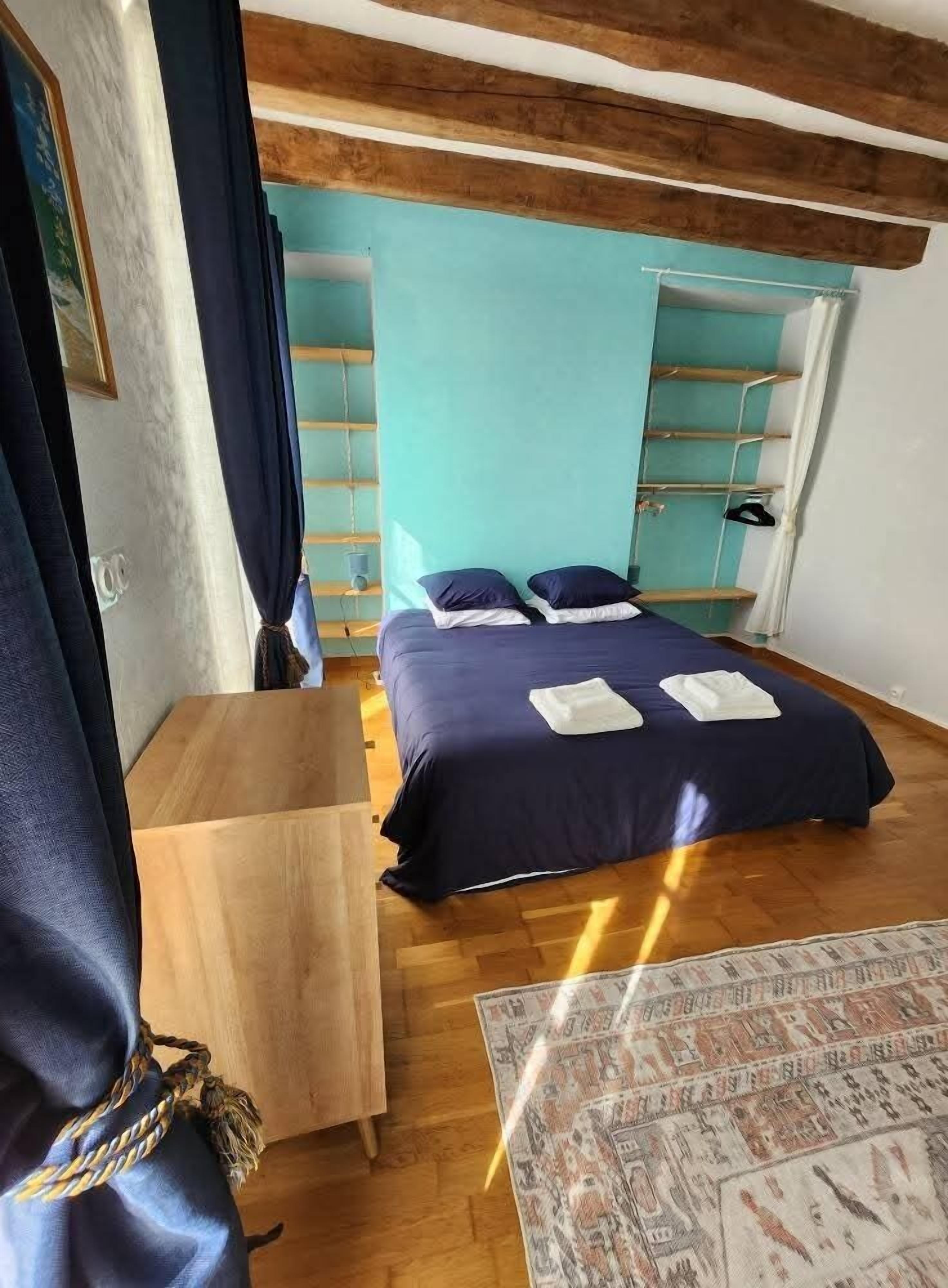 Ein Schlafzimmer mit einem Bett, einem hölzernen Nachttisch, einer blauen Wand und einem gemusterten Teppich.