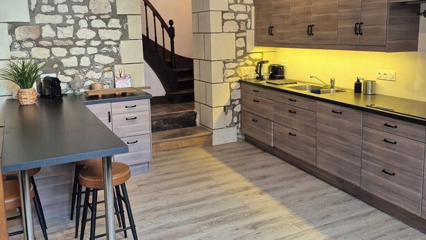 Eine Küche mit Steinwänden, Holzbalken und einer Bar mit Hockern.