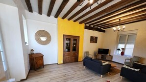 Ein Wohnzimmer mit Holzboden, einer gelben Akzentwand und einem Fernseher. Es gibt ein Holzschränkchen und einen roten Sessel.
