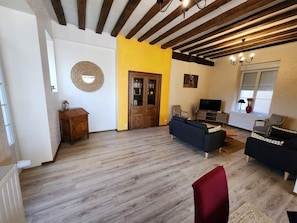A living room with wooden flooring, a yellow accent wall, and a TV. There is a wooden cabinet and a red chair. - Maison de village entre le futuroscope et Beauval (Preuilly-sur-Claise)
