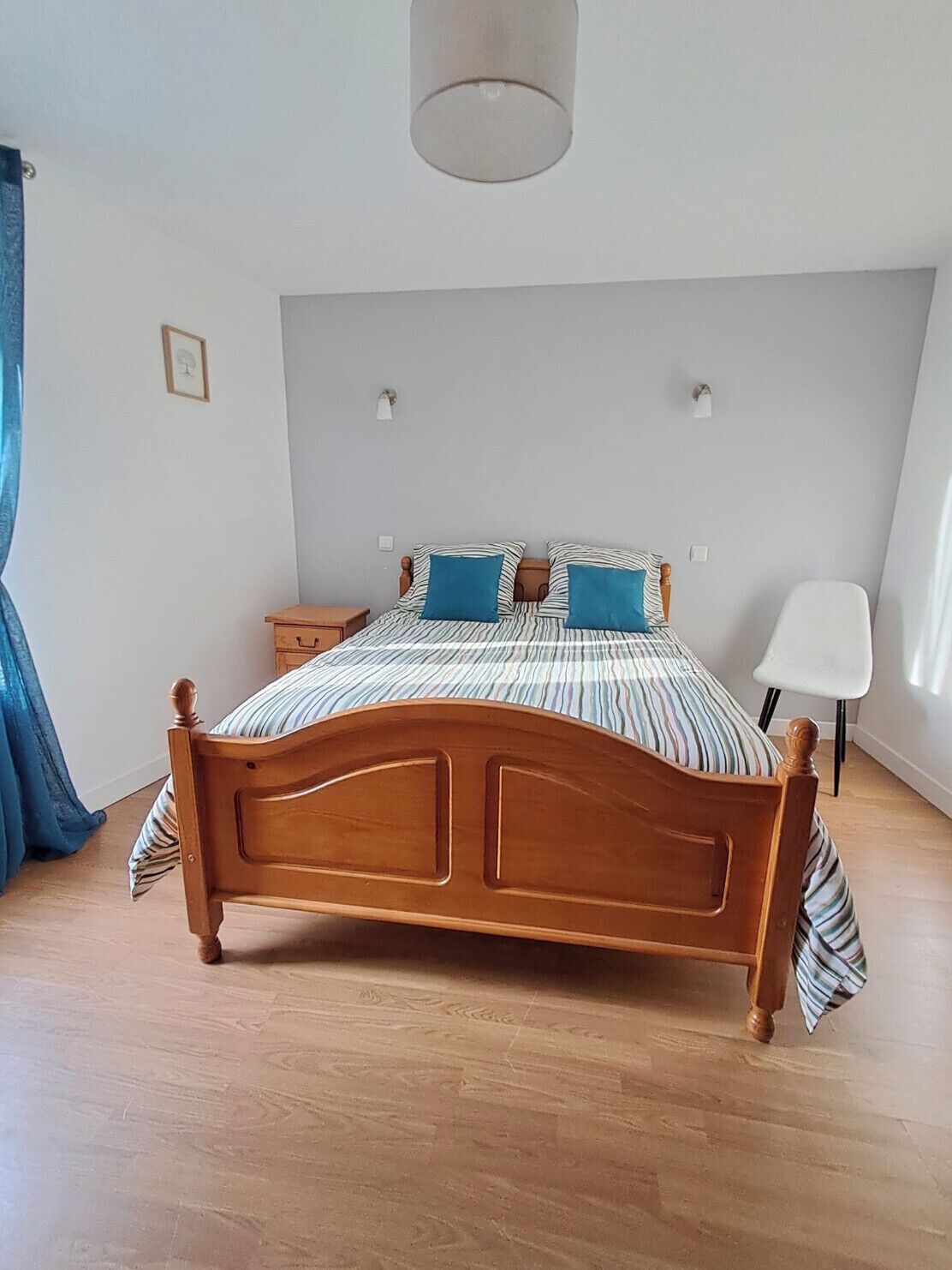 A bedroom with a wooden bed, striped bedding, and two wall-mounted lamps.