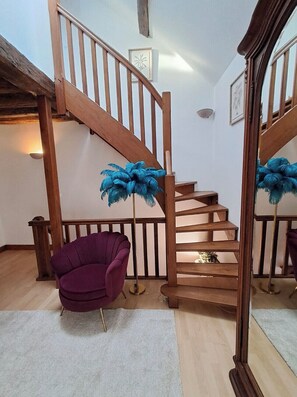 Una escalera con barandillas de madera y un sillón púrpura en una habitación con paredes blancas y suelo de madera.