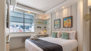 A bedroom with a bed, a window, a shelf with decorative items, and a painting on the wall. - Charm in Copacabana Stc1002 (Rio de Janeiro)