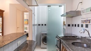 A modern kitchen with granite countertops, a built-in oven, and a washing machine in the adjacent room. - Charm in Copacabana Stc1002 (Rio de Janeiro)