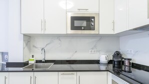 Eine moderne Küche mit weißen Schränken, einer schwarzen Arbeitsplatte, einer eingebauten Mikrowelle, einer Kaffeemaschine und einem Wasserkocher.