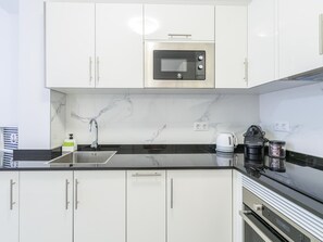 A modern kitchen with white cabinets, a black countertop, a built-in microwave, a coffee maker, and a kettle. - CHL Casa Los Cancajos, sea and peace in La Palma (Breña Baja)