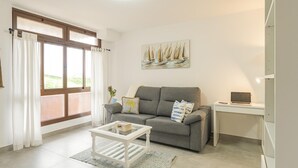 Ein Wohnzimmer mit grauem Sofa, einem weißen Couchtisch, einem Segelbootgemälde an der Wand und einem Schreibtisch mit einem Laptop.