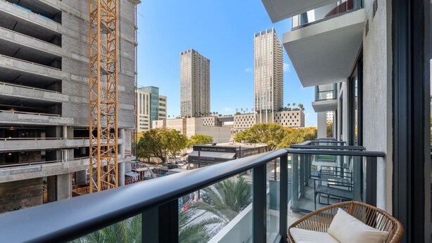 A balcony with a wicker chair, overlooking a construction site and high-rise buildings. - Crosby Miami WTC 1BR/1BA Cozy #304 (Miami)