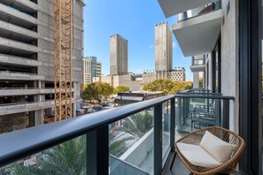Varanda com cadeira de vime, com vista para um canteiro de obras e edifícios altos.