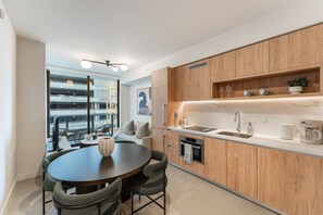 A modern kitchen with wooden cabinets, a built-in oven, and a dining area with a round table and chairs. - Crosby Miami WTC 1BR/1BA Cozy #304 (Miami)