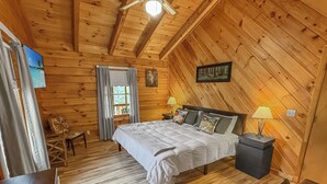 A cozy wooden cabin bedroom with a bed, two bedside lamps, a chair, and a small table. - Relax @ Benny Bear Cabin, WNC's newest addition • 2 Bed 2 Bath • Family Friendly (Bryson City)