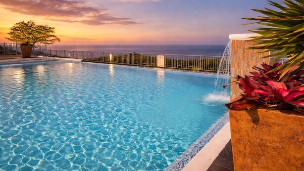 A swimming pool with clear water, a waterfall feature, and a view of the ocean at sunset. - Pyramid Tranquility/Luxury Retreat in Ocho Rios, St. Ann (Ocho rios)
