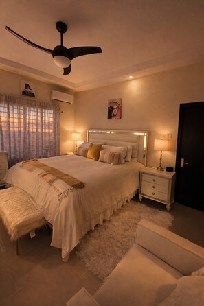 A bedroom with a bed, bedside tables, a nightstand, a ceiling fan, and a door. - Pyramid Tranquility/Luxury Retreat in Ocho Rios, St. Ann (Ocho rios)