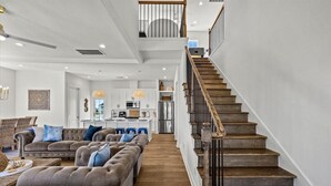 Ein geräumiges Wohnzimmer mit einer großen Eckcouch, einer Holztreppe und einer Küche im Hintergrund.