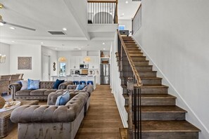 A spacious living room with a large sectional sofa, a wooden staircase, and a kitchen in the background.