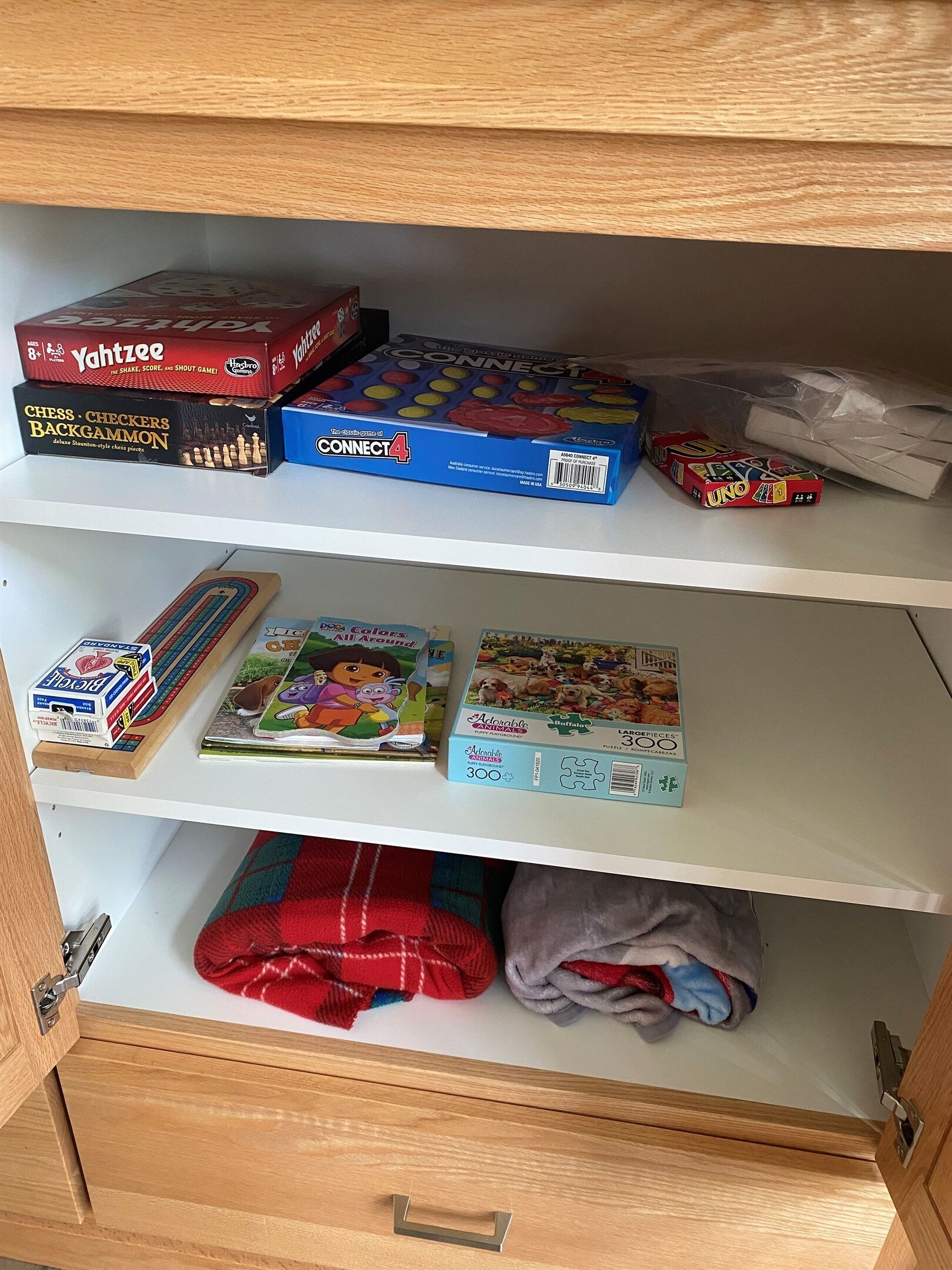 Una estantería con diversos juegos de mesa y rompecabezas, incluyendo Yahtzee, Connect4 y un rompecabezas de 300 piezas con temática animal.